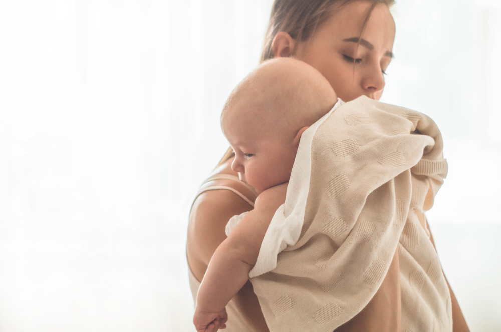 Home portrait of a newborn baby with mother on the bed. Mom holding and kissing her child. Concept breast feeding.