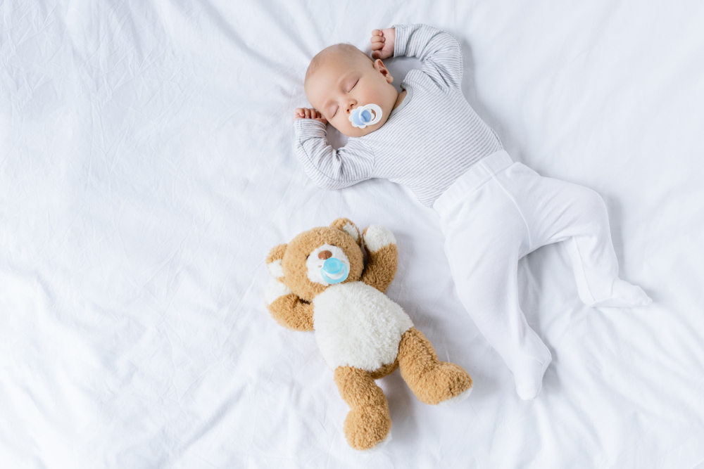 overhead view of cute baby with pacifier sleeping on bed with teddy bear